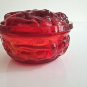 May include: A red glass bowl with a floral design. The bowl is made of clear glass with a red tint. The bowl is decorated with a floral design that is raised from the surface of the bowl.