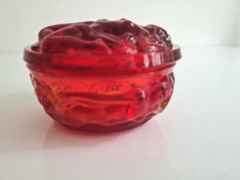 May include: A red glass bowl with a floral design. The bowl is made of clear glass with a red tint. The bowl is decorated with a floral design that is raised from the surface of the bowl.