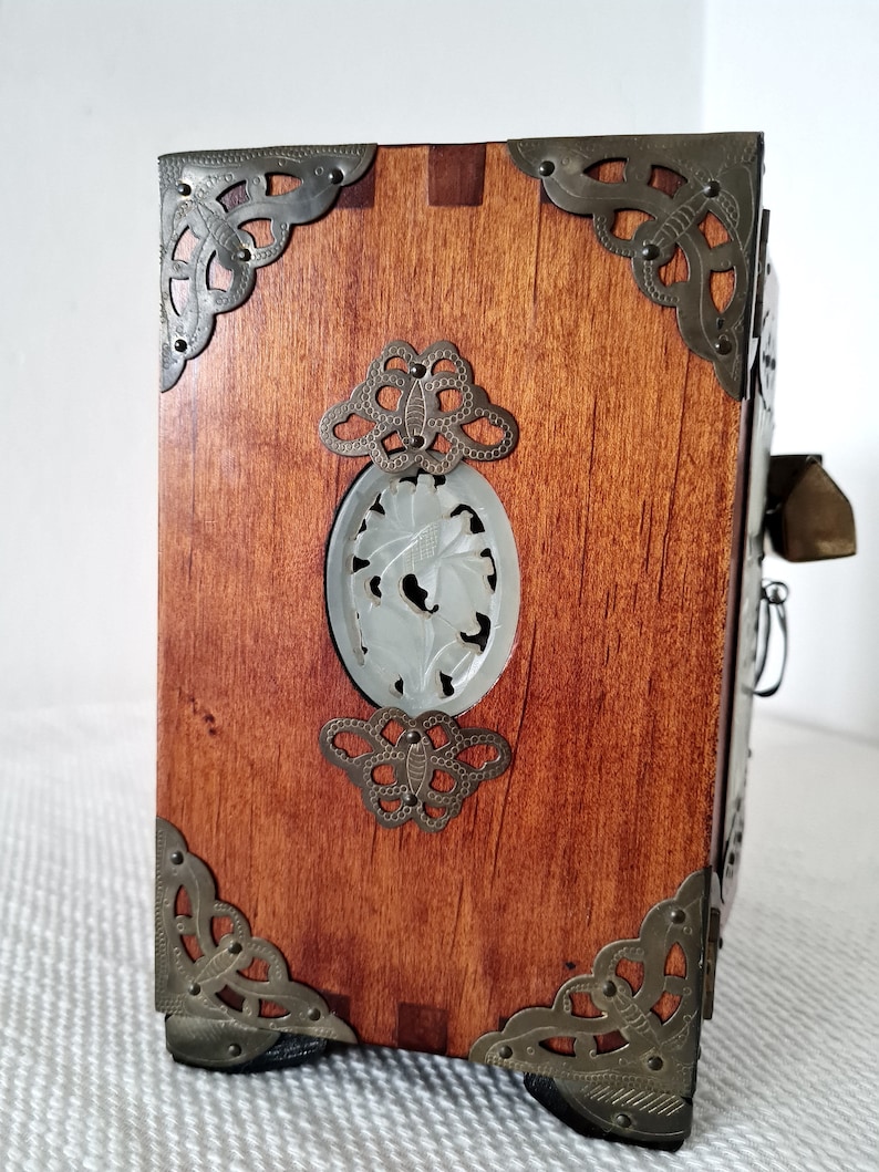 May include: A wooden box with ornate metal corners and a carved jade panel on the front. The box has a dark brown stain and is decorated with intricate metalwork.