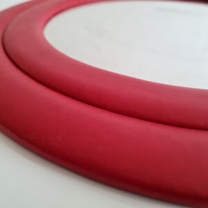 May include: A close-up of a red round mirror with a double-layered frame.