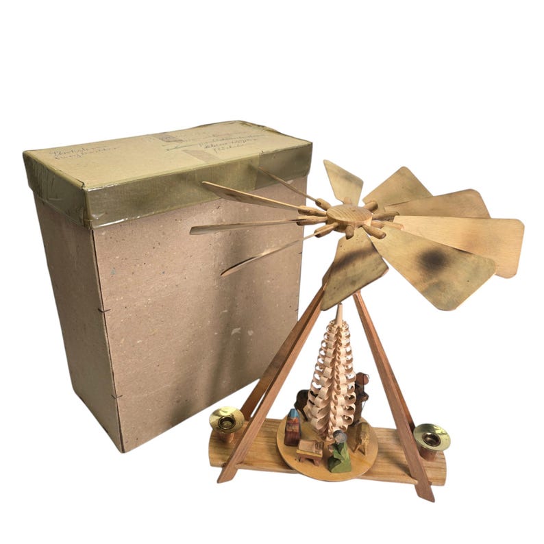 May include: A wooden Christmas pyramid with a star-shaped top and a rotating fan. The pyramid features a nativity scene with figures of Mary, Joseph, and the baby Jesus. The pyramid is in its original box.