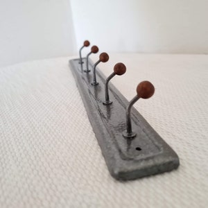 Puede incluir: Un colgador de metal plateado con seis ganchos. Cada gancho tiene una bola de madera marrón en el extremo.
