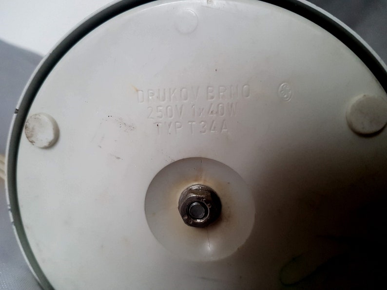 May include: White base of a vintage electric appliance with the text "DRUKOV BRNO 250V 1x40W TYP T34A" printed on it.