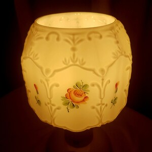 May include: A white ceramic lampshade with a floral design. The lampshade has a scalloped edge and is decorated with painted roses and leaves.