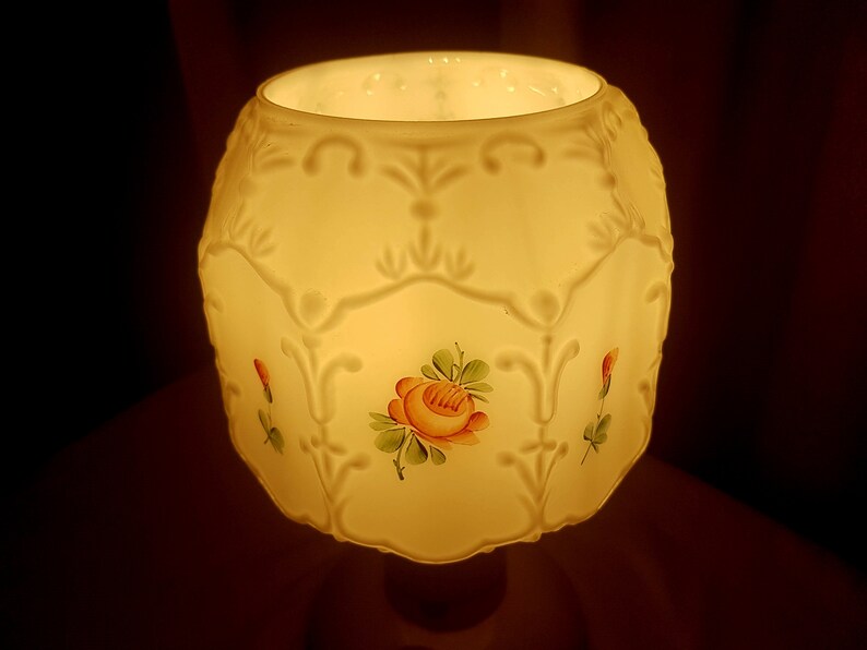 May include: A white ceramic lampshade with a floral design. The lampshade has a scalloped edge and is decorated with painted roses and leaves.