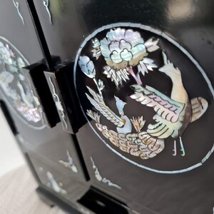 May include: Black wooden cabinet with intricate mother-of-pearl inlay depicting a pair of birds and a flower. The cabinet has two doors and multiple drawers.