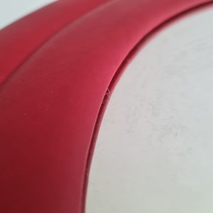May include: Close-up of a red leather edge of a circular object. The edge is curved and has a smooth, polished finish.