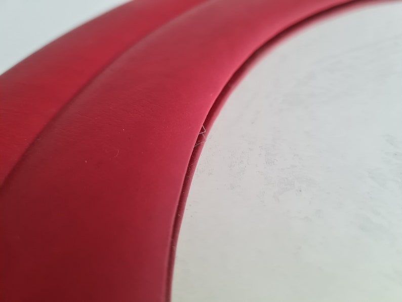 May include: Close-up of a red leather edge of a circular object. The edge is curved and has a smooth, polished finish.