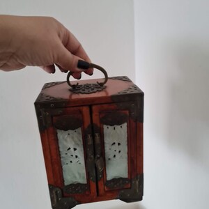 May include: A small wooden box with two doors and a brass handle. The doors are decorated with carved designs and have a translucent white material behind them.