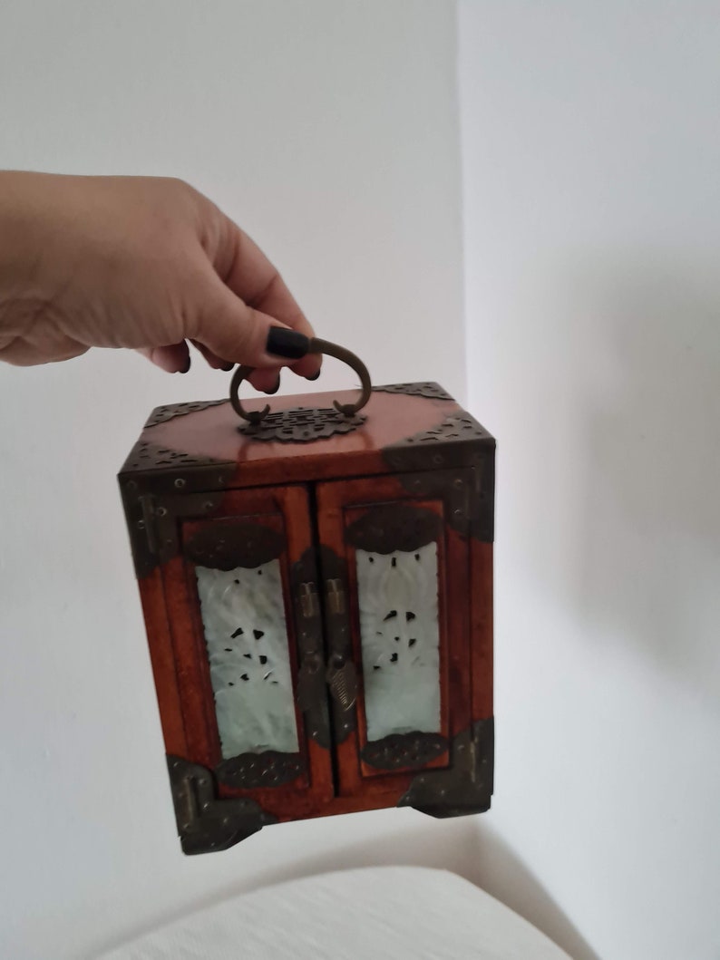 May include: A small wooden box with two doors and a brass handle. The doors are decorated with carved designs and have a translucent white material behind them.