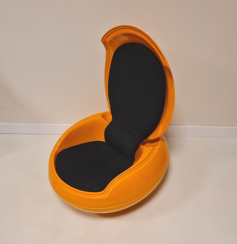 May include: A bright orange egg-shaped chair with a black fabric seat and a curved back. The chair is open and ready to be sat in.