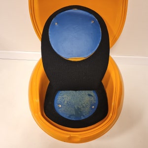 May include: A yellow egg-shaped chair with a black and blue padded seat. The chair is open and the top half is flipped back.