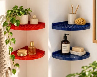 May include: Two sets of two-tier corner shelves, one set in glossy red and one set in glossy navy blue. The shelves feature a ribbed surface design for drainage. The red shelves hold a potted plant and a glass perfume bottle, while the blue shelves hold a toothbrush holder, a natural sponge, a pump bottle of Aesop body cleanser, and a bar of soap in a speckled dish.