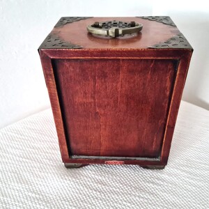 May include: A wooden box with a brass handle and decorative metal accents. The box is closed and has a dark brown finish.
