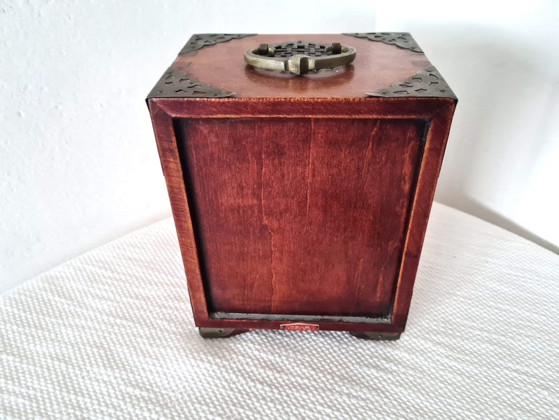May include: A wooden box with a brass handle and decorative metal accents. The box is closed and has a dark brown finish.
