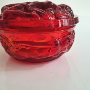 May include: A red glass trinket dish with a decorative design of stylized flowers. The dish has a rounded shape and a smooth, glossy finish.