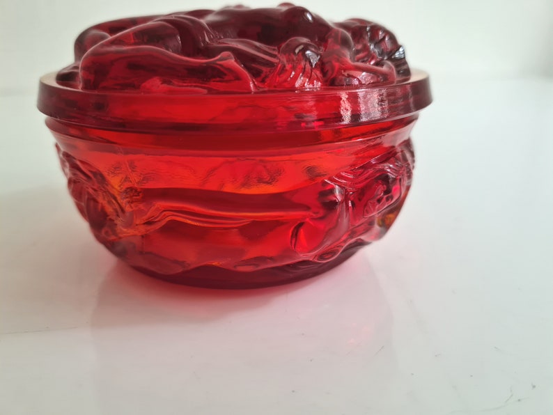 May include: A red glass trinket dish with a decorative design of stylized flowers. The dish has a rounded shape and a smooth, glossy finish.