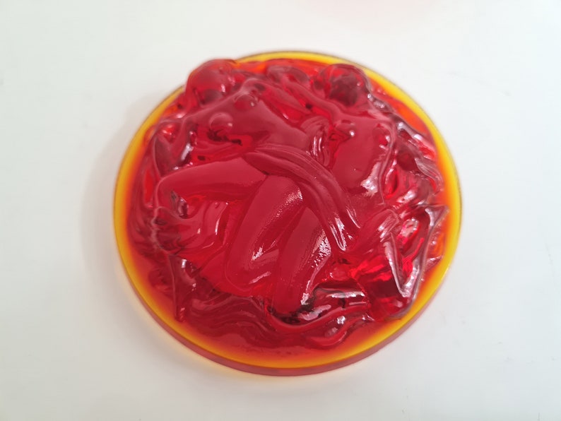 May include: A red glass paperweight with a swirling design. The paperweight is set in a clear glass base with a yellow rim.