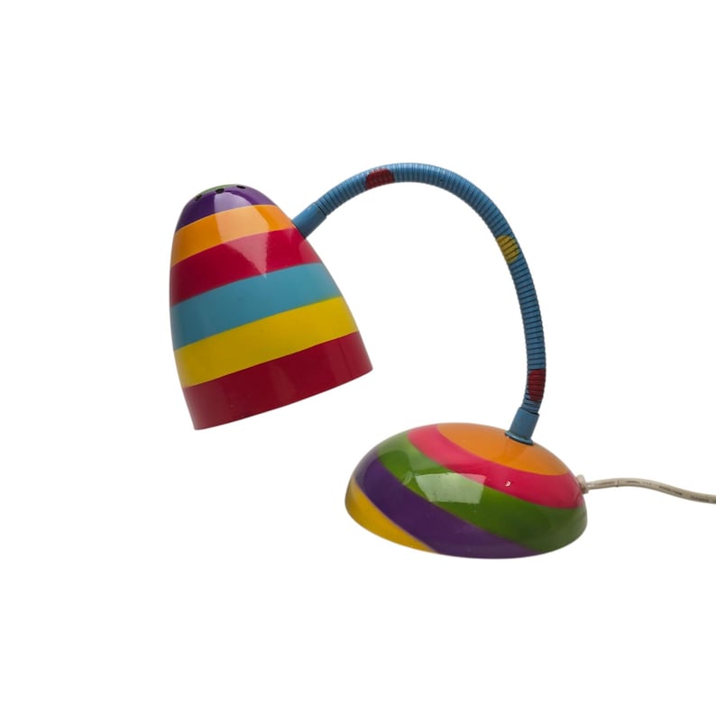 May include: A colorful desk lamp with a striped design. The lamp features a cone-shaped shade and a rounded base, both adorned with vibrant stripes in red, yellow, blue, and green. The flexible neck is blue.
