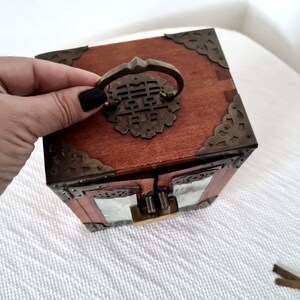 May include: A wooden box with a brass latch and intricate carvings. The box has a glass front and a brass handle with a Chinese character on it.