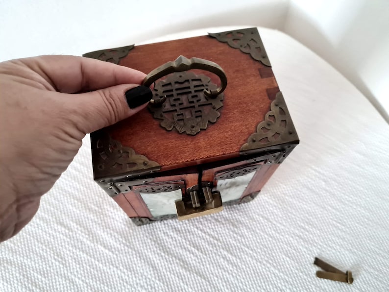 May include: A wooden box with a brass latch and intricate carvings. The box has a glass front and a brass handle with a Chinese character on it.