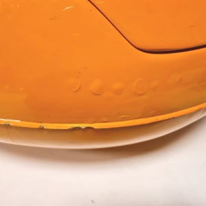 May include: Close-up of a bright orange, round, plastic toy with a slight dent on the surface.