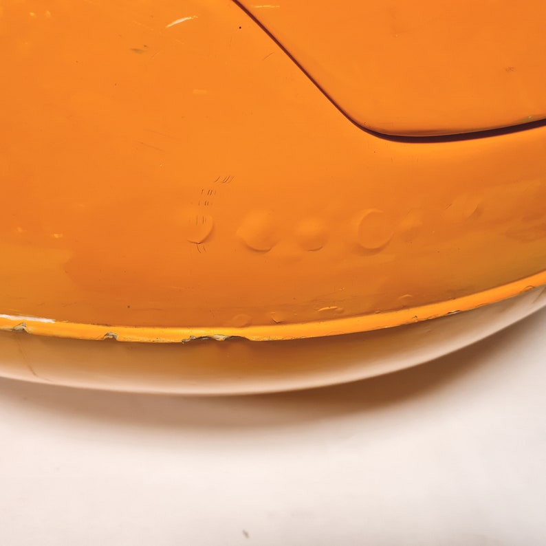 May include: Close-up of a bright orange, round, plastic toy with a slight dent on the surface.