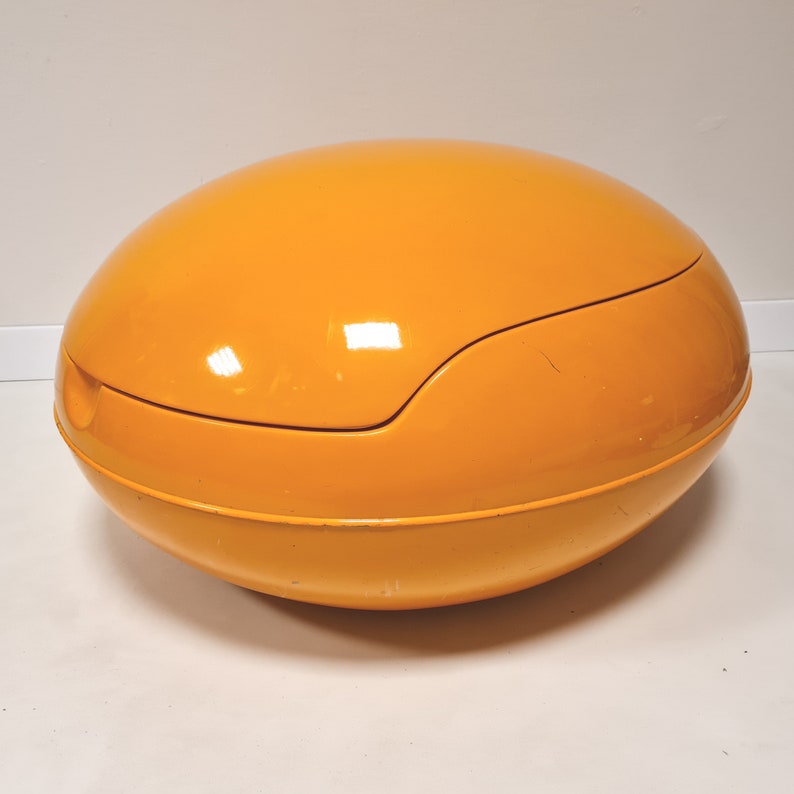 May include: A bright orange, egg-shaped storage ottoman with a smooth, glossy finish.