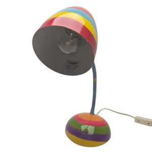 May include: A colorful desk lamp with a striped design. The lamp features a red, yellow, blue, and green striped lampshade and base. The flexible neck is blue with a yellow stripe. The lamp has a white power cord and a switch.