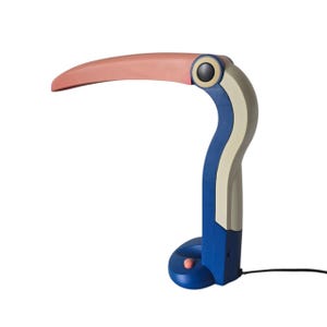 May include: A whimsical desk lamp shaped like a toucan. The lamp features a curved, pink beak, a blue and white body, and a round base with a pink button. The lamp is connected to a black power cord.