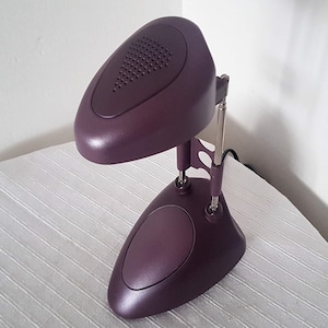 May include: A purple desk lamp with a unique, rounded design. The lamp has a flexible arm and a small, round base.