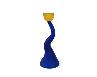 May include: A tall, wavy candle holder featuring a matte blue finish on the curved, elongated body and a contrasting matte yellow cup at the top. The base is wide and circular, tapering into a slender, serpentine neck that supports the candle cup.