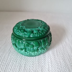 May include: A green glass trinket box with a carved design of flowers and bows. The lid is closed.