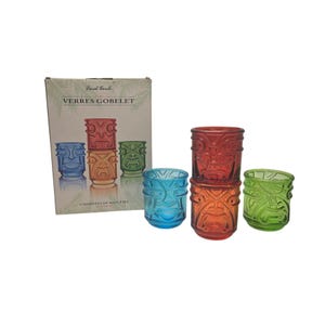 May include: A set of four colorful Tiki-style glasses in red, orange, green, and blue. The glasses are arranged with three stacked and one separate. The box in the background reads "VERRES GOBELET" and "4 MODÈLES DE DIEU TIKI".