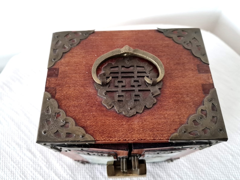 May include: A wooden box with a brass handle and decorative corners. The handle is shaped like a ring and has a Chinese character in the center. The box is closed.