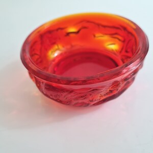 May include: A small, red glass bowl with a textured, raised design. The bowl is made of clear glass with a red tint.