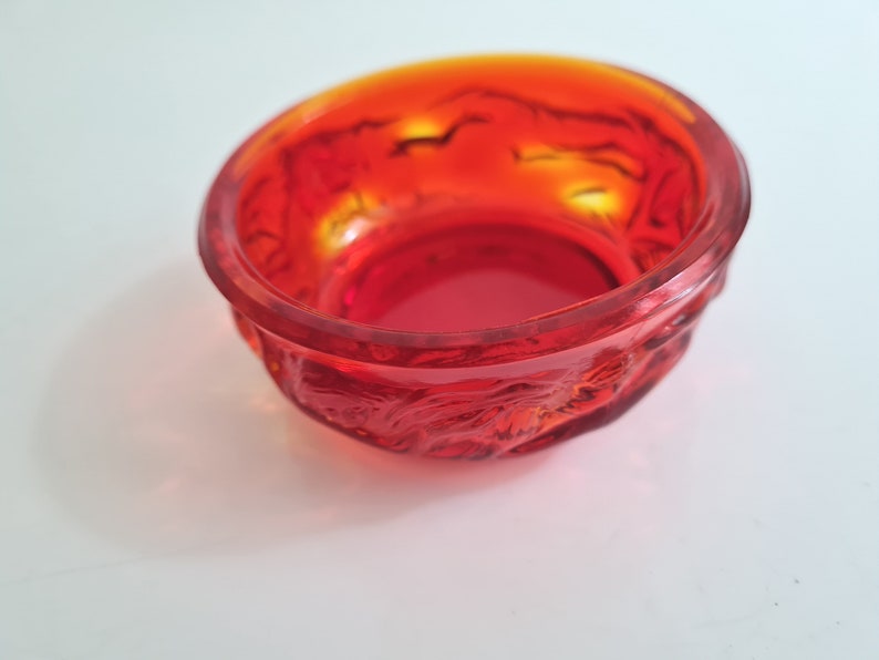 May include: A small, red glass bowl with a textured, raised design. The bowl is made of clear glass with a red tint.