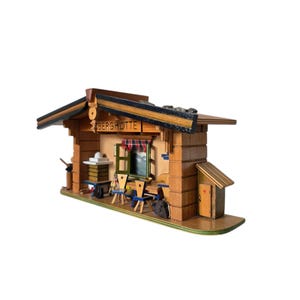 Könnte beinhalten: Ein Holzmodell einer Berghütte mit einem Schild, auf dem "Berghütte" steht. Die Hütte hat ein Fenster mit Blick auf eine Bergszene und einen kleinen Tisch und Stühle auf der Veranda.