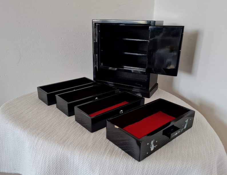 May include: Black wooden jewelry box with a hinged lid and four pull-out drawers. The drawers have red felt lining and are decorated with a floral design.