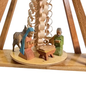 May include: A wooden nativity scene with a carved wooden tree, a donkey, a man and a woman kneeling in prayer. The scene is set on a wooden base.