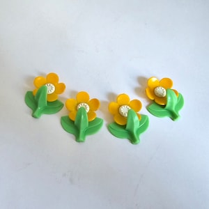 May include: Four yellow flower-shaped hooks with green leaves. The hooks are made of plastic and have a white centre.