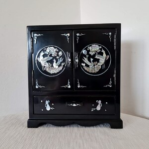May include: A black wooden jewelry box with two doors and a drawer. The doors and drawer are decorated with mother-of-pearl inlays of birds and flowers.