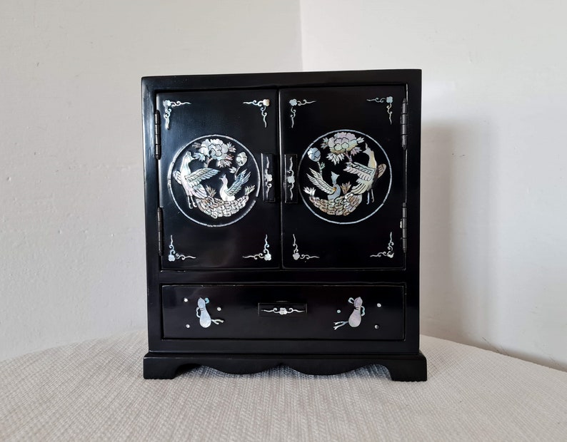May include: A black wooden jewelry box with two doors and a drawer. The doors and drawer are decorated with mother-of-pearl inlays of birds and flowers.