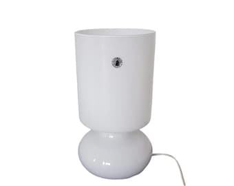 May include: White glass table lamp with a round base and a cylindrical shade. The lamp has a cord and a switch.