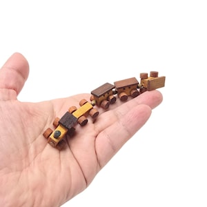 Op de afbeelding: Een houten speelgoedtrein met vier wagons, elk geverfd in tinten bruin en geel. De trein ligt op een hand, met de locomotiefwagen vooraan en de laatste wagon achteraan.