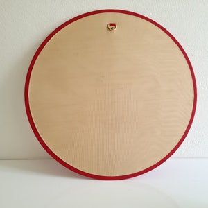 May include: A round, wooden canvas with a red border and a gold hanging loop. The canvas is blank and ready for painting.