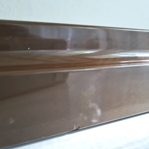 Puede incluir: Primer plano de una superficie rectangular marr&oacute;n y brillante con una ligera curva en el borde superior.