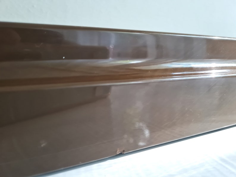 Puede incluir: Primer plano de una superficie rectangular marr&oacute;n y brillante con una ligera curva en el borde superior.
