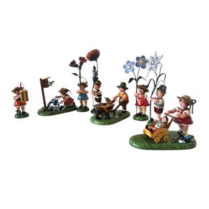 Könnte beinhalten: Eine Sammlung von Miniaturfiguren, die Kinder bei verschiedenen Gartenaktivitäten darstellen. Die Figuren sind in traditioneller Kleidung gekleidet und auf grünen Sockeln angeordnet. Die Szene zeigt Kinder mit Blumen, einer Schubkarre und einem Kinderwagen.