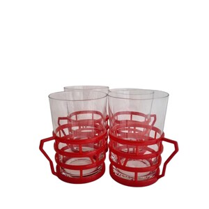 May include: Set of four clear glass drinking glasses with red plastic handles. The handles are a cage-like design that wraps around the glass.